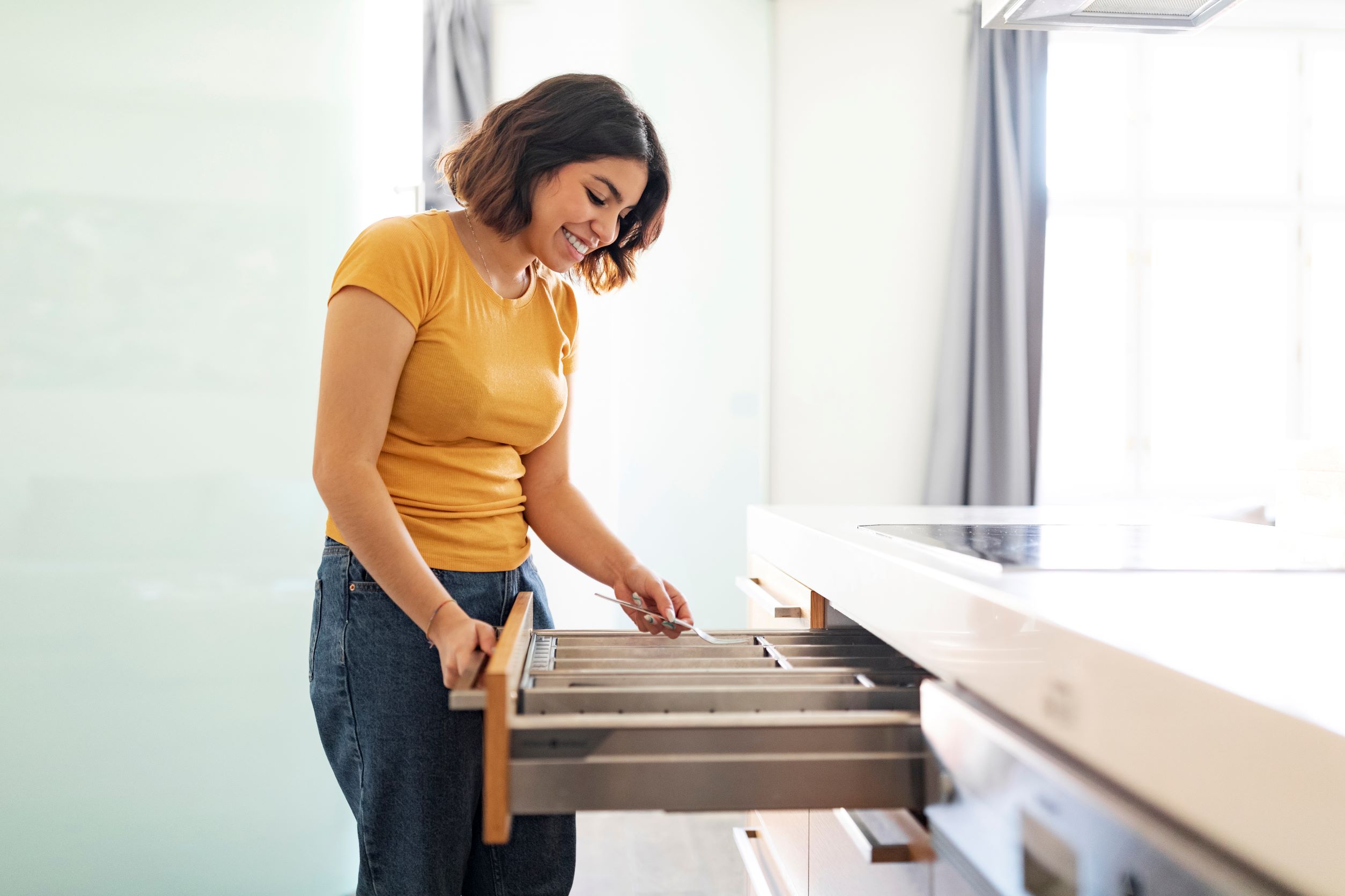 Young women opening a cabinet drawer and grabbing a utensil. One of the key benefits of cabinet drawers is their ability to maximize storage space