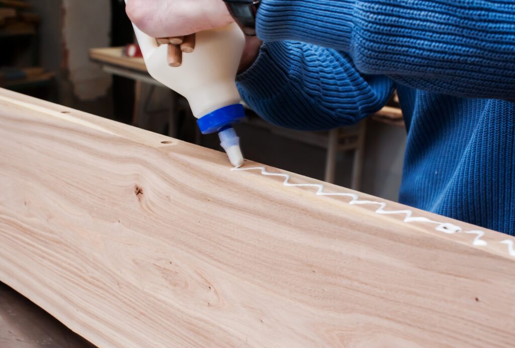 Man applying glue to wood and gluing boards in carpentry workshop