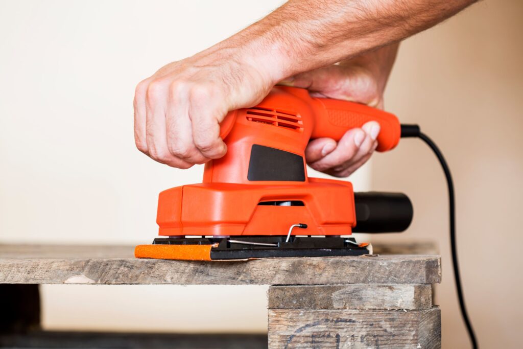 Man Hands using and orange and black sanding apparatus  with 400 grit sandpaper