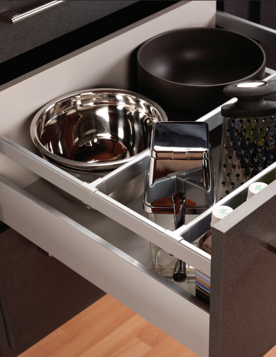 Open kitchen drawer showing metal bowls a chrome coffee press a grater and a black mixing bowl arranged in divider sections