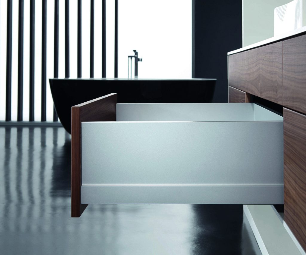 Low angle view of a modern gray dresser with open drawers wood trim and a dark backdrop in a minimalist interior