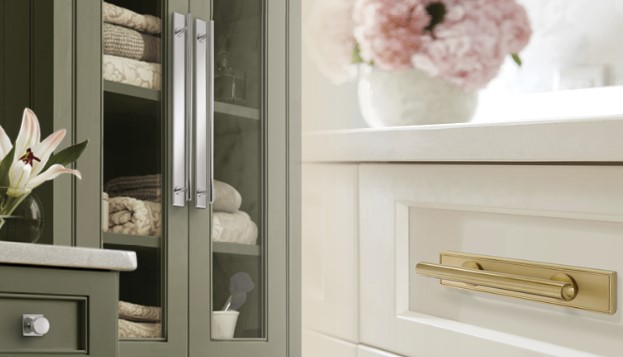 ThoreauBackplates Woodworker Express Blog Open dark green cabinet with glass doors showing folded towels and a marble countertop beside a white dresser with a gold handle and pink flowers in the background