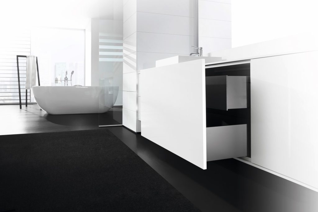 Modern minimalist bathroom with a freestanding oval tub near a large window white cabinetry and a dark rug on the floor