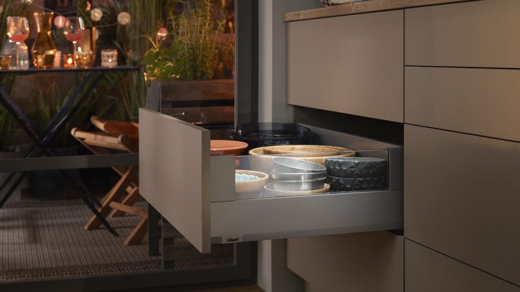 Open pull out drawer showing a stack of ceramic bowls in beige gray and black in a modern grey kitchen edge