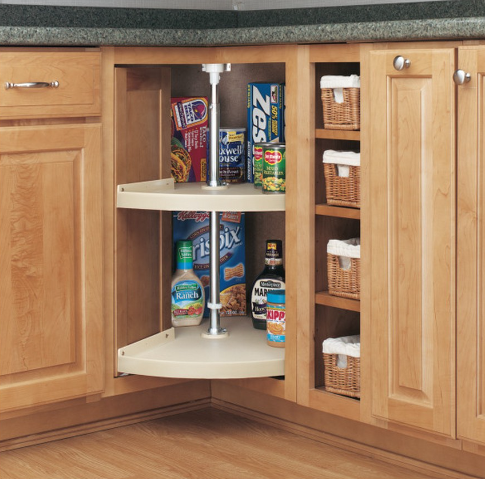 Corner kitchen cabinet with a rotating two tier Lazy Susan storing pantry items like cereal boxes and canned goods with wicker baskets on adjacent shelves