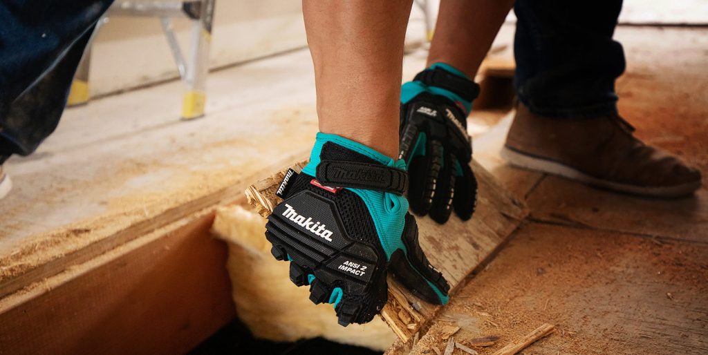 Cut Resistant Gloves for Woodworking Woodworker Express Blog Person wearing teal and black Makita protective gloves places a rough wooden board on a work surface at a construction site