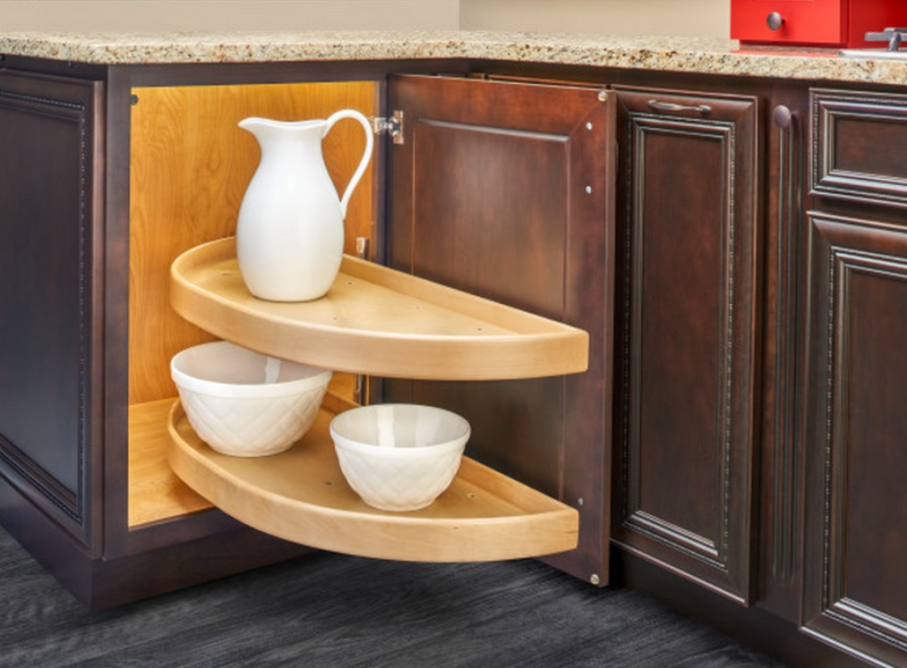Curved wooden pull out shelf in a dark kitchen cabinet with a white pitcher on the top tier and two white bowls on the lower tier